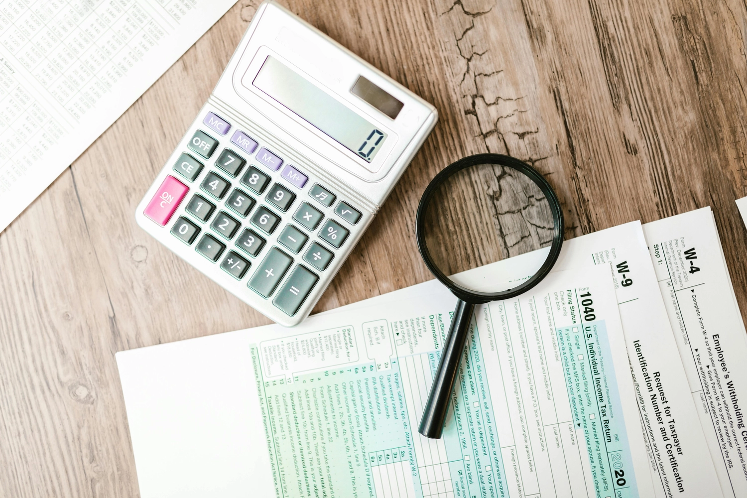BIM - Bayerisches InvestManagement - InvestManagement - Ein Taschenrechner und eine Lupe liegen neben Steuerunterlagen auf einer Holzfläche.